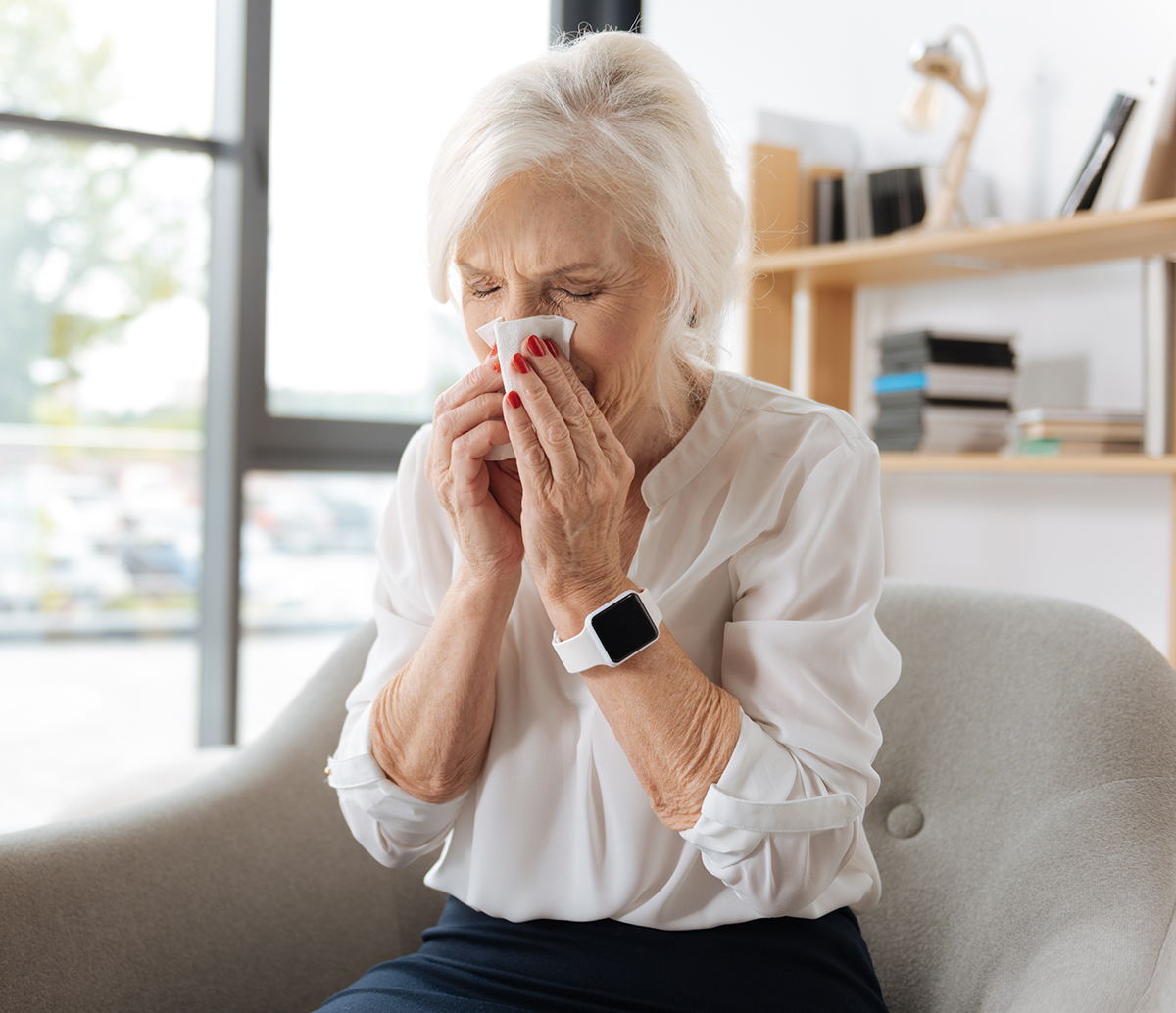 Catching a cold. Unhappy moody elderly woman holding a paper tissue and sneezing while having a cold