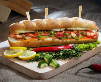 photo of sub sandwhich filled with shrimp peppers cheese and hot sauces sitting on cutting board dressed with lemon slices and long red chile peppers