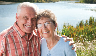 senior man and senior woman standing for photo with a large body of water in the background